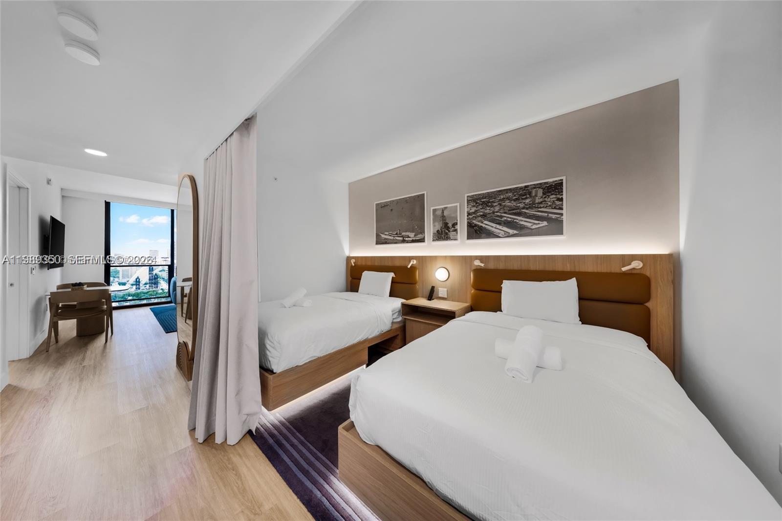 A bedroom features two beds, a wooden headboard, a curtain divider, and a city view — 159 NE 6 ST # 1617, Miami FL 33132, MIAMI, FL