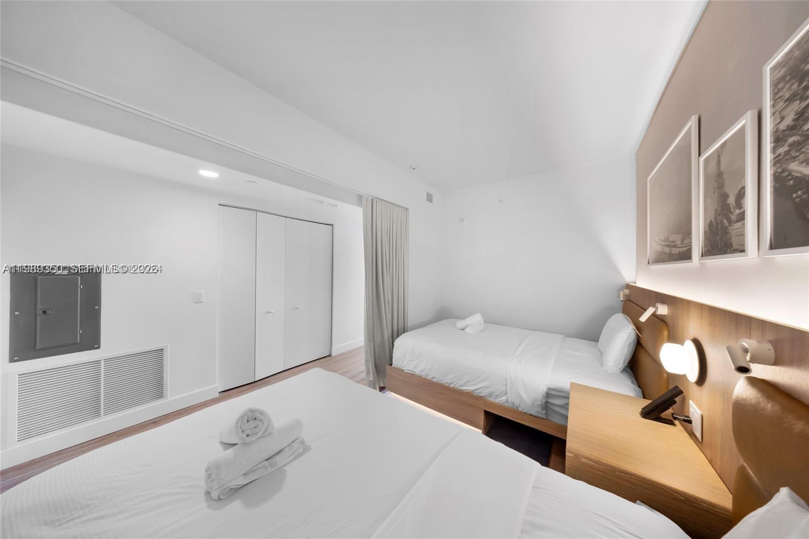 A bedroom features two beds, a wooden headboard with integrated lighting, and white walls — 159 NE 6 ST # 1617, Miami FL 33132, MIAMI, FL