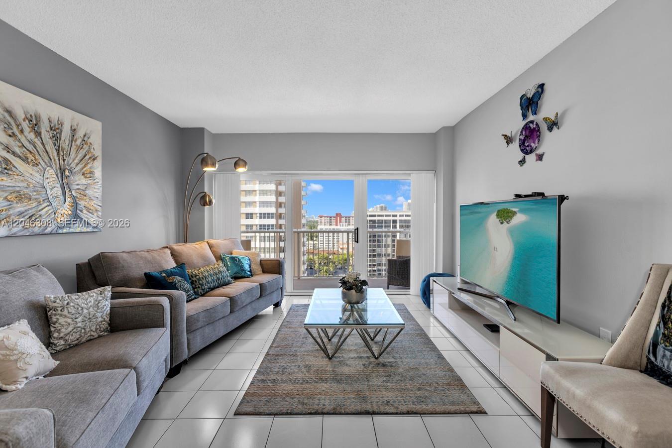 A living room features a gray sofa, glass coffee table, television, and a balcony view — 1965 S Ocean Dr # 14C, Hallandale Beach FL 33009, HALLANDALE BEACH, FL