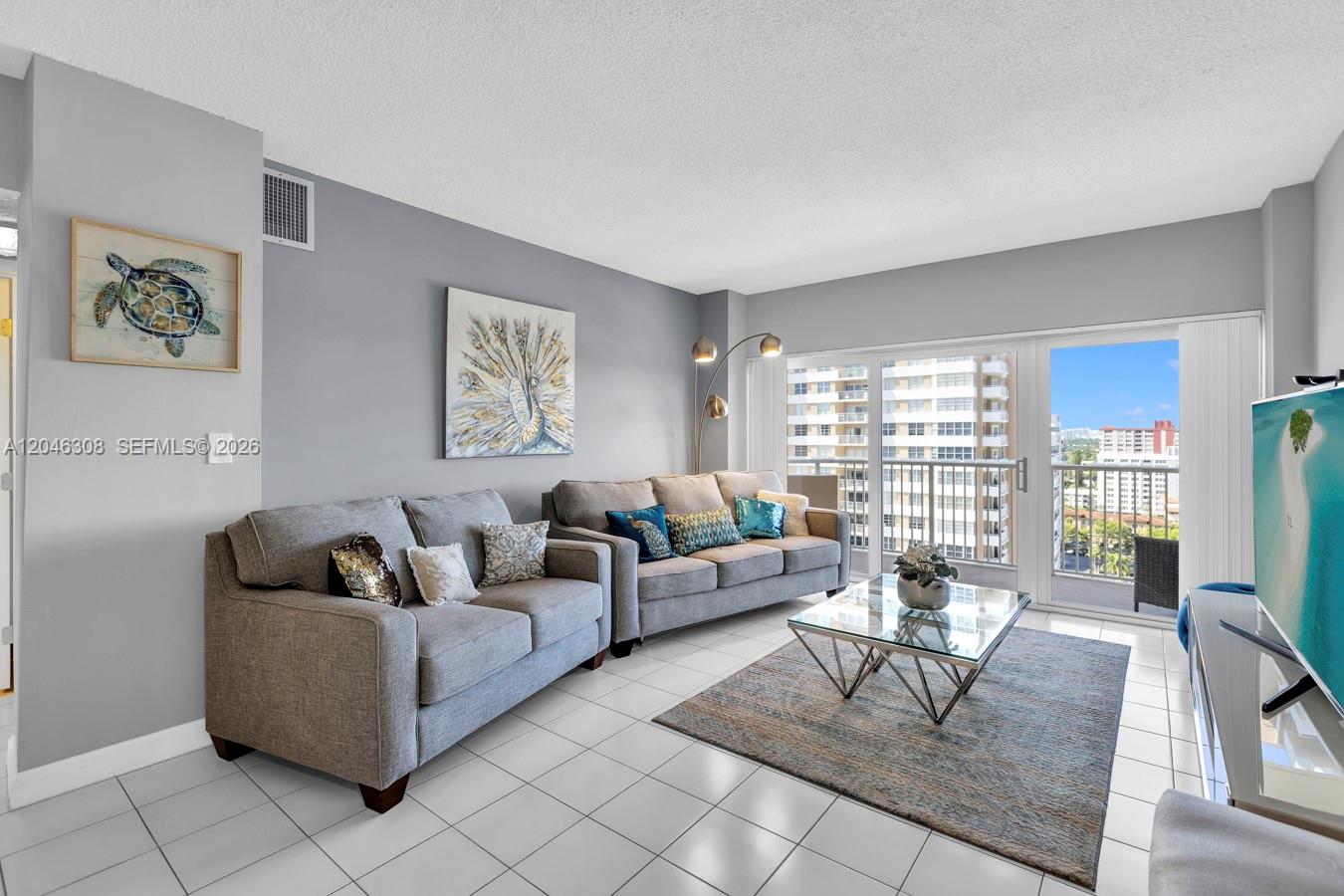 A living room features two gray sofas, a glass coffee table, and a balcony view — 1965 S Ocean Dr # 14C, Hallandale Beach FL 33009, HALLANDALE BEACH, FL