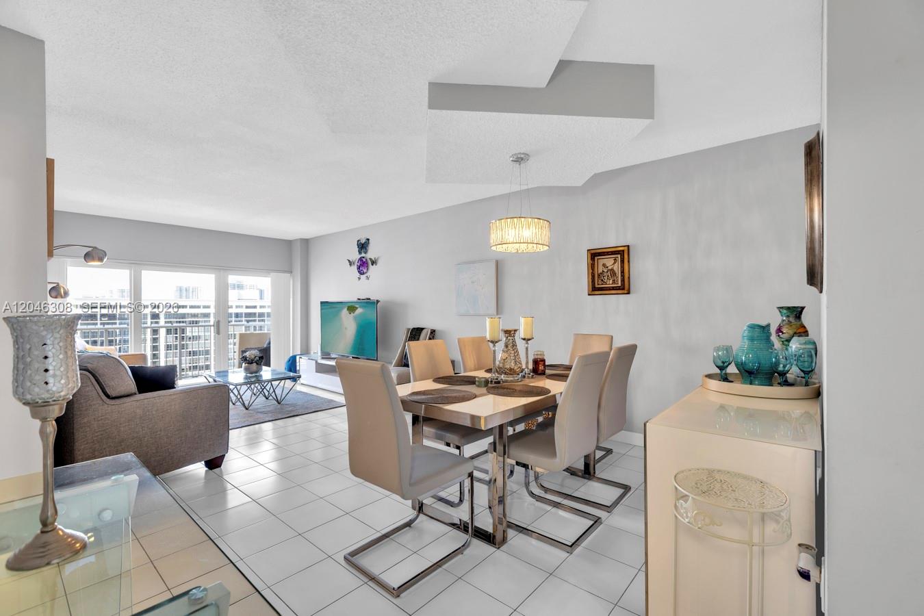 A dining area and living room feature white tile floors, neutral furniture, and a balcony view — 1965 S Ocean Dr # 14C, Hallandale Beach FL 33009, HALLANDALE BEACH, FL