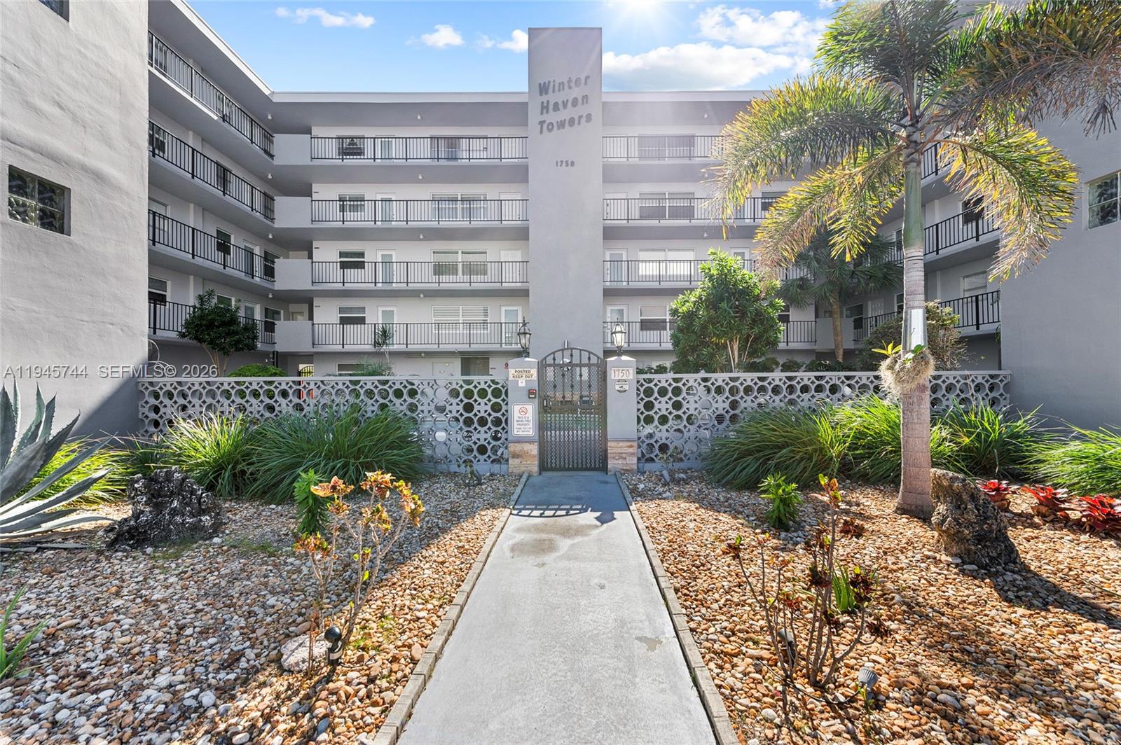 The exterior of a multi-story apartment building features a central entrance gate and landscaping — 1750 Jefferson St # 510, Hollywood FL 33020, HOLLYWOOD, FL