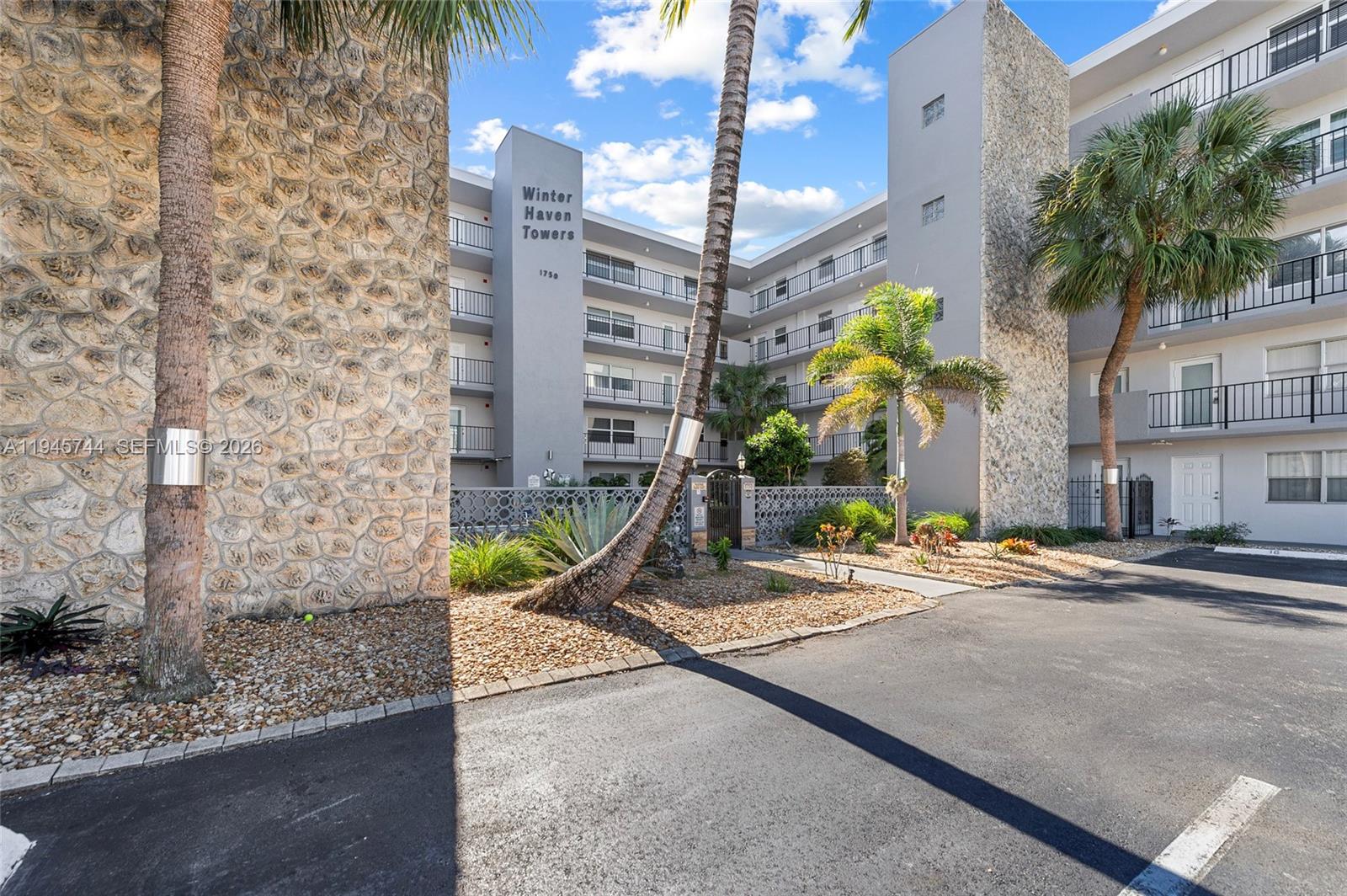 The exterior of a multi-story apartment building features stone-clad pillars and palm trees — 1750 Jefferson St # 510, Hollywood FL 33020, HOLLYWOOD, FL