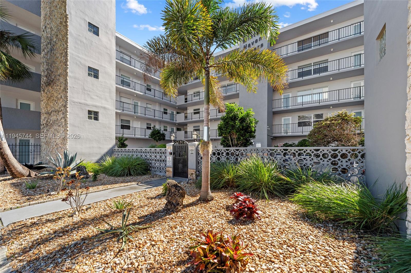 A multi-story apartment building features a gated entrance, palm trees, and a gravel courtyard — 1750 Jefferson St # 510, Hollywood FL 33020, HOLLYWOOD, FL