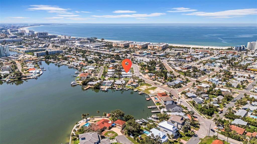 This aerial view shows a coastal neighborhood with houses, a canal, and the ocean beyond — 6855 GULF WINDS DRIVE, ST PETE BEACH, FL