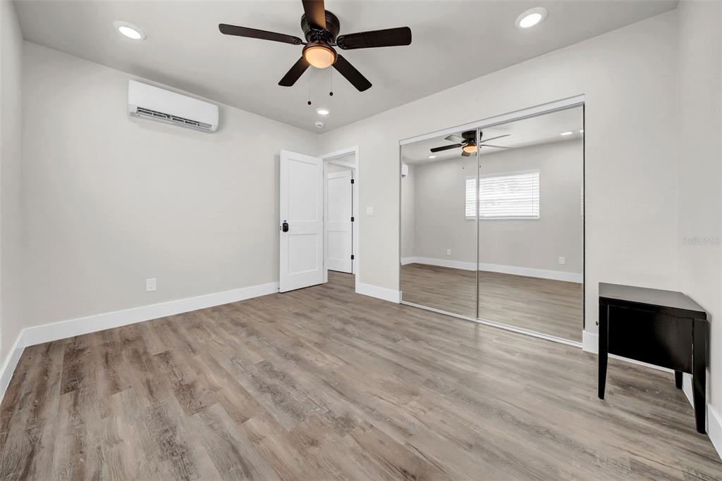 A bedroom with light gray walls, wood-look flooring, a ceiling fan, and mirrored closet doors — 6855 GULF WINDS DRIVE, ST PETE BEACH, FL