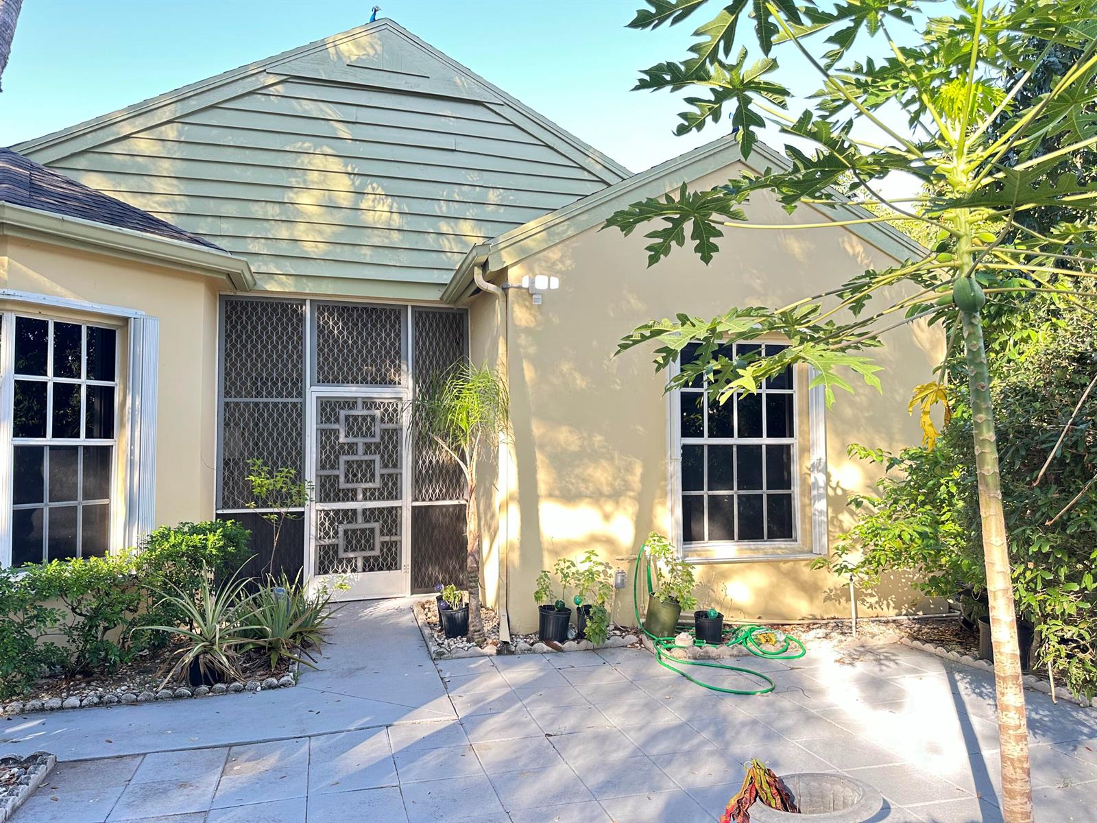 The exterior of a light yellow house features a screened front door and a paved patio — 7729 Forest Green Lane, Boynton Beach FL 33436, BOYNTON BEACH, FL