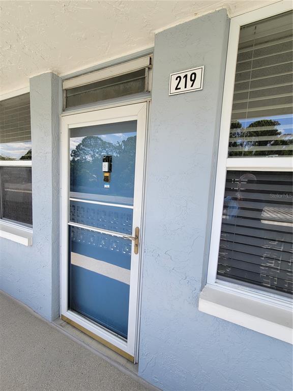 A light blue exterior wall features a white door with a storm door and number 219 — 4720 LOCUST STREET NE UNIT 219, ST PETERSBURG, FL