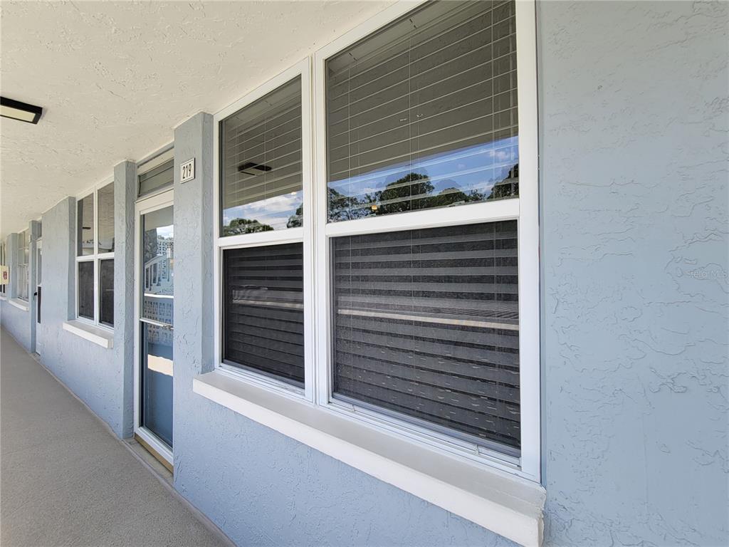 A view of a building exterior with a walkway, blue stucco walls, and windows — 4720 LOCUST STREET NE UNIT 219, ST PETERSBURG, FL