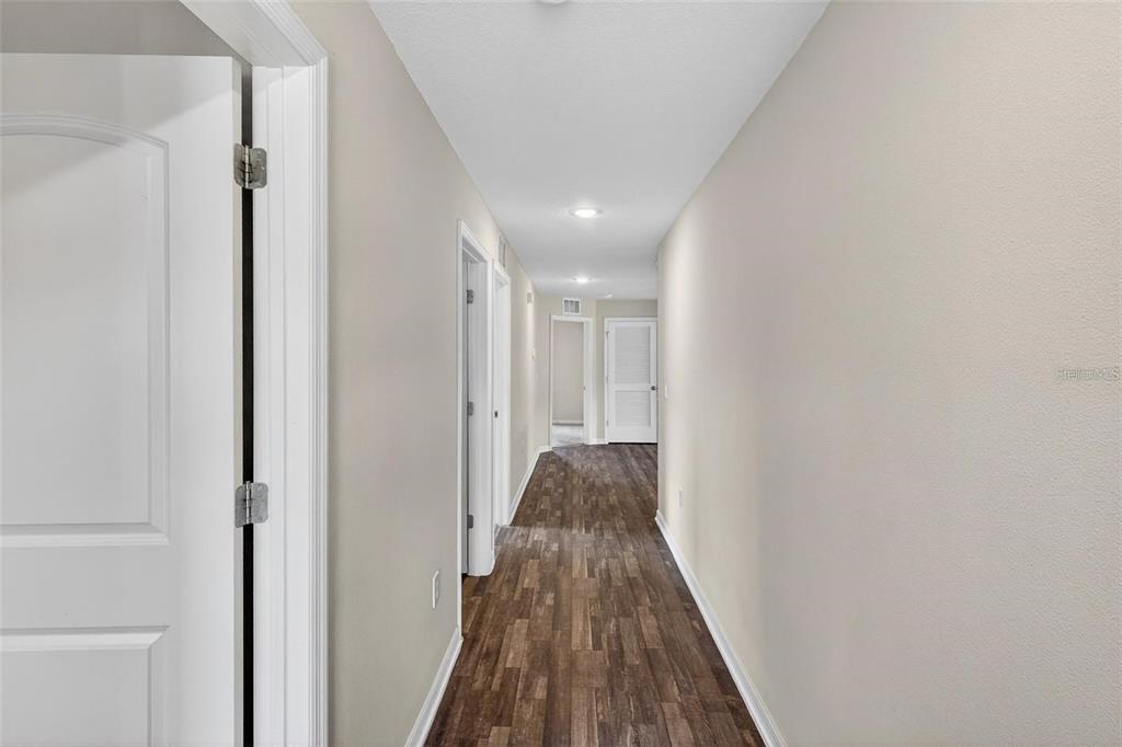 A hallway with light-colored walls and dark wood-look flooring leads toward a distant doorway — 842 GILA WAY, KISSIMMEE, FL