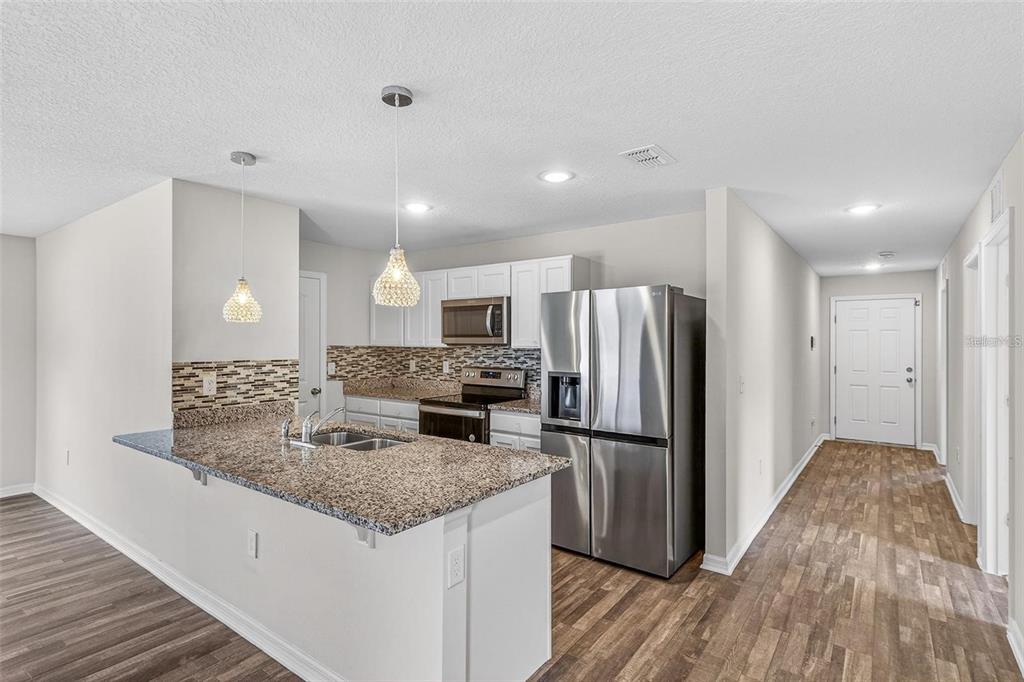 A kitchen features white cabinets, granite countertops, stainless steel appliances, and wood-look flooring — 842 GILA WAY, KISSIMMEE, FL