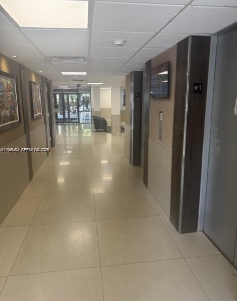 A brightly lit hallway features light tile flooring, elevator doors, and framed artwork on the walls — 4164 Inverrary Dr # 913, Lauderhill FL 33319, LAUDERHILL, FL