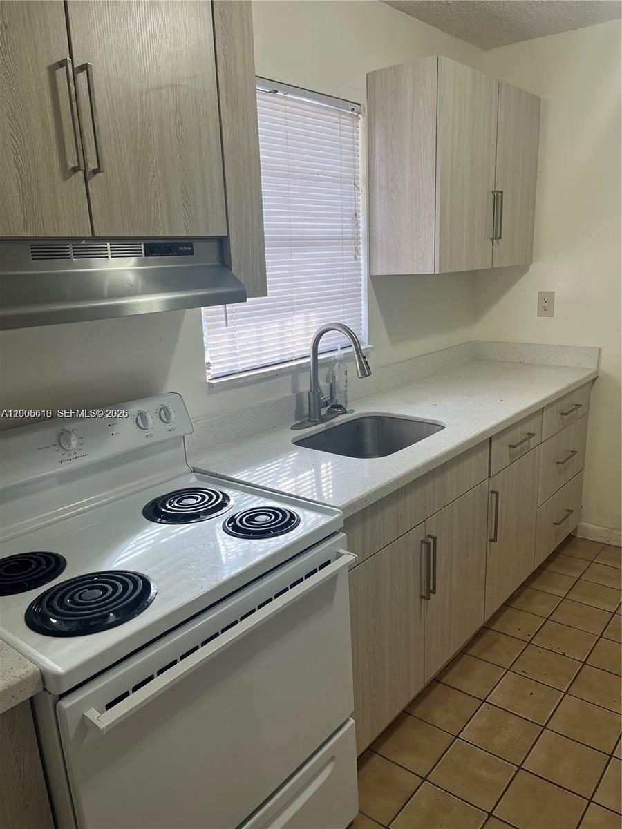 A kitchen features light wood-grain cabinets, white countertops, a white electric stove, and tiled floors — 2255 W 55th St # 2, Hialeah FL 33016, HIALEAH, FL