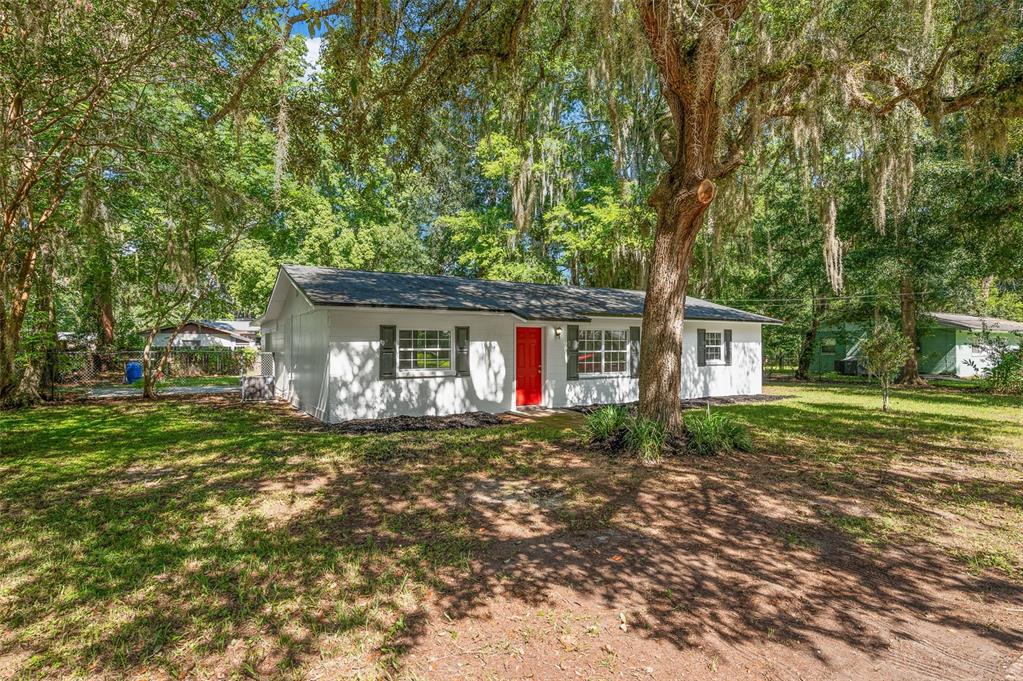 A white single-story house with a red front door sits on a grassy, tree-shaded lot — 2100 SE 50TH STREET, GAINESVILLE, FL