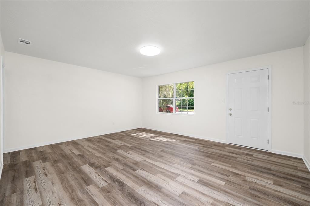 An empty room with light-colored walls, wood-look flooring, a single window, and a white door — 2100 SE 50TH STREET, GAINESVILLE, FL