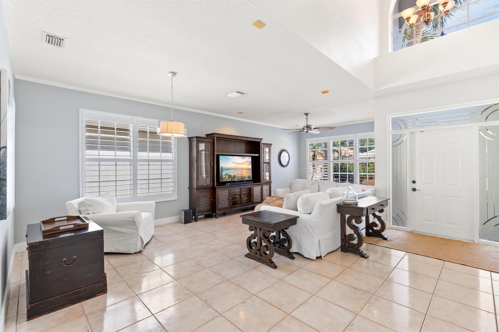 A living room features light tile floors, white furniture, a dark wood entertainment center, and windows — 7611 Doubleton Drive, Delray Beach FL 33446, DELRAY BEACH, FL