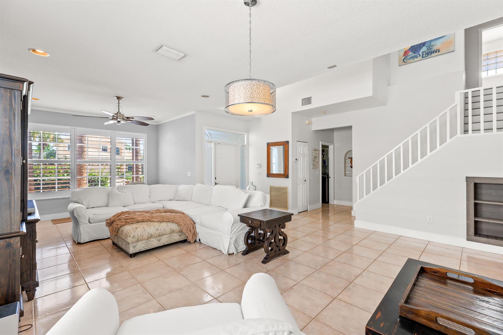 A bright living room features a white sectional sofa, tile flooring, and a staircase — 7611 Doubleton Drive, Delray Beach FL 33446, DELRAY BEACH, FL