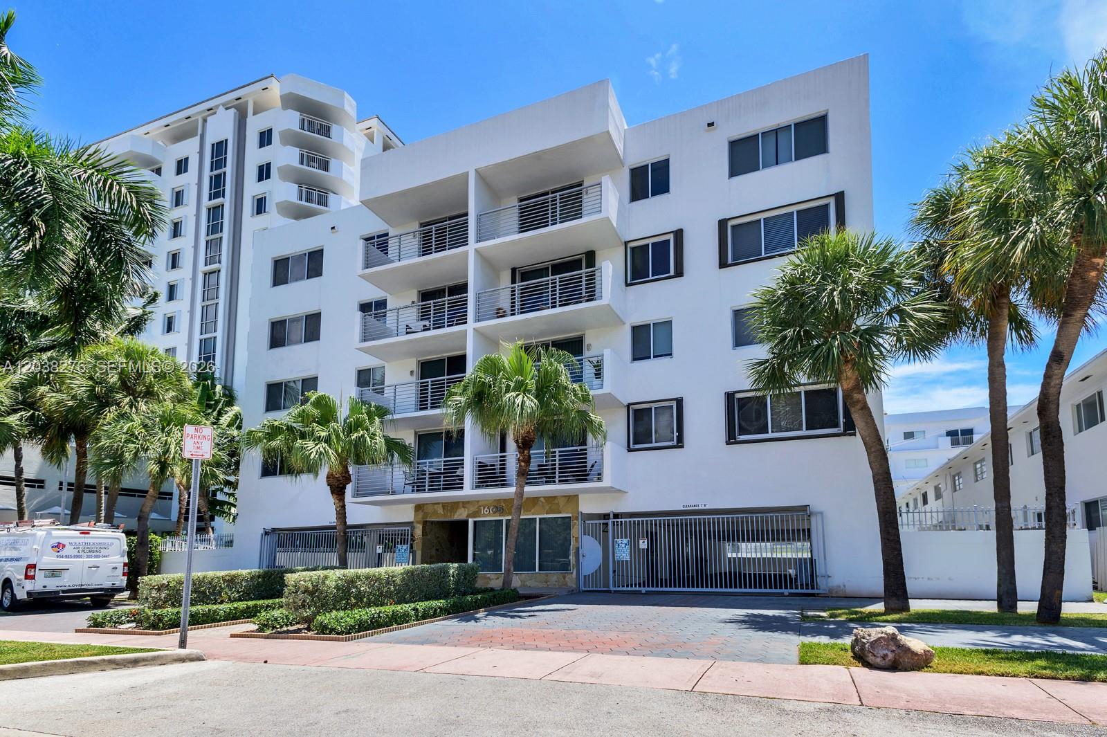 A multi-story white apartment building features balconies and a gated ground-level parking entrance — 1605 Bay Rd # 308, Miami Beach FL 33139, MIAMI BEACH, FL