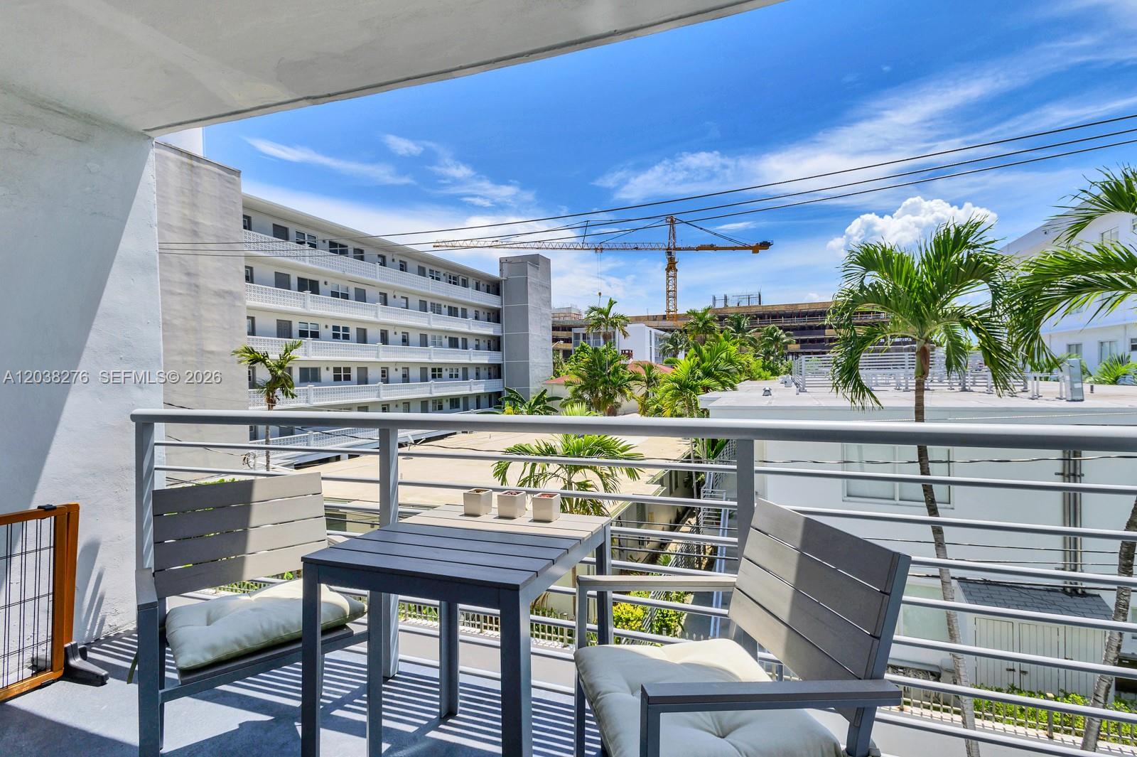 A balcony features a small table and two chairs overlooking a neighboring building and crane — 1605 Bay Rd # 308, Miami Beach FL 33139, MIAMI BEACH, FL
