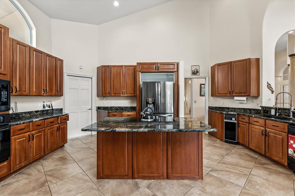 A kitchen with wood cabinets, dark granite countertops, a central island, and tile flooring — 1036 GOLF VALLEY DRIVE, APOPKA, FL