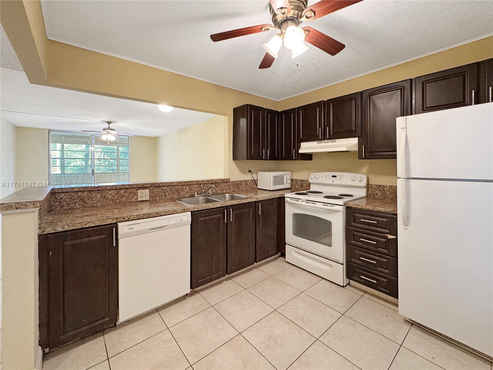 A kitchen features dark wood cabinets, white appliances, granite countertops, and light-colored floor tiles — 410 NW 68th Ave # 207, Plantation FL 33317, PLANTATION, FL