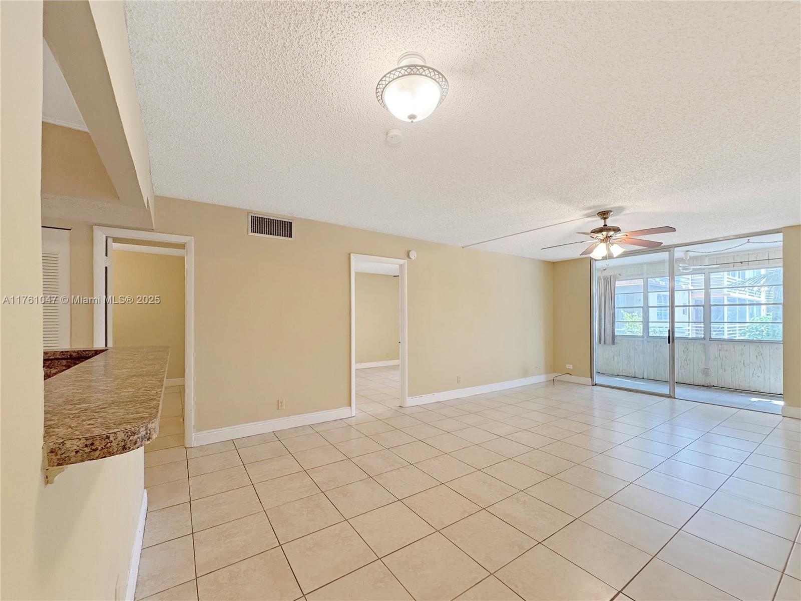 A spacious living room features beige tile floors, a ceiling fan, and a sliding glass door — 410 NW 68th Ave # 207, Plantation FL 33317, PLANTATION, FL