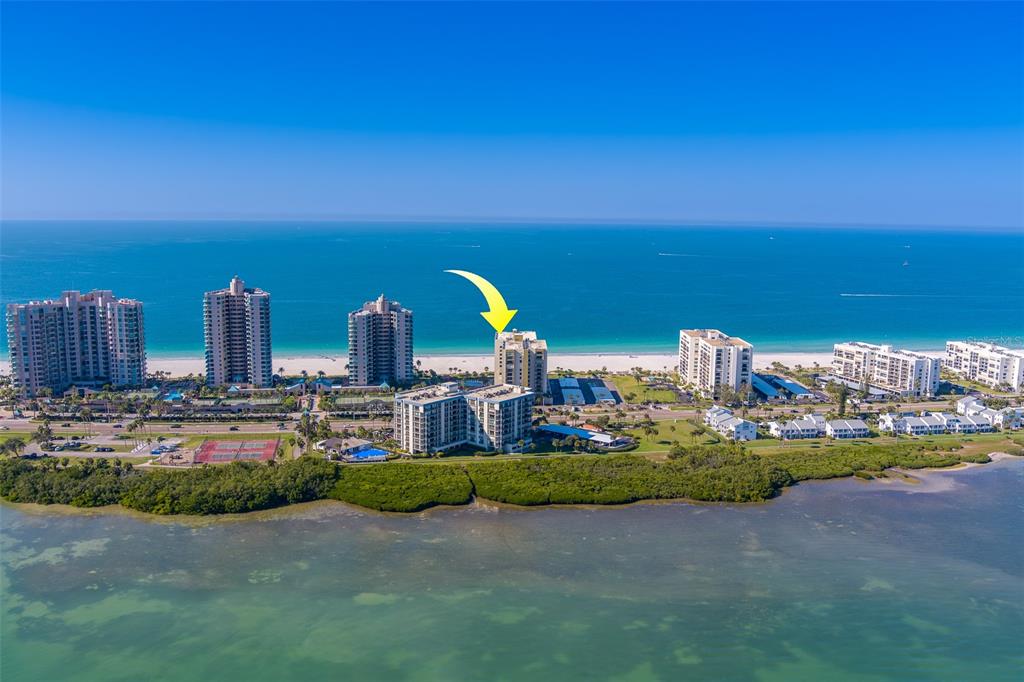 An aerial view shows high-rise beachfront condominiums along a coastline with a yellow arrow pointing down — 1480 GULF BOULEVARD UNIT 201, CLEARWATER BEACH, FL