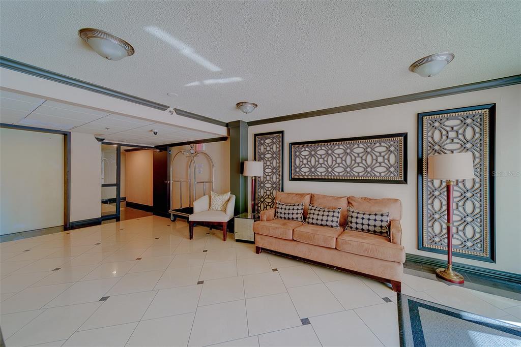 A lobby area features a tan sofa, decorative wall panels, tile flooring, and a luggage cart — 1480 GULF BOULEVARD UNIT 201, CLEARWATER BEACH, FL