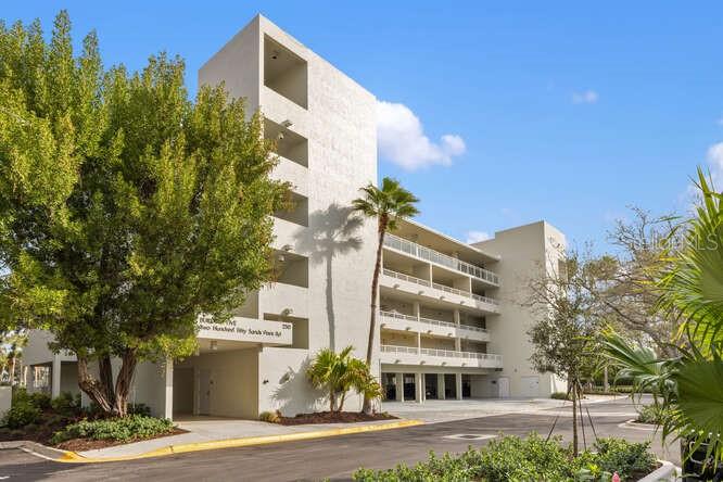 A multi-story white apartment building with balconies and a large tree in the foreground — 250 SANDS POINT ROAD UNIT 5203, LONGBOAT KEY, FL
