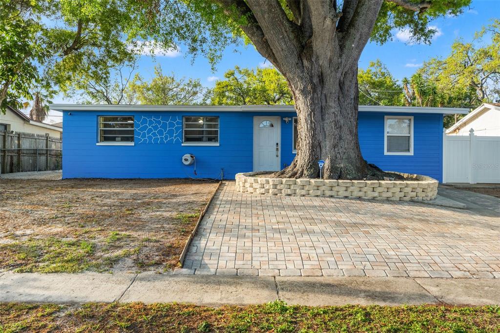 A bright blue single-story house features a large tree with a stone planter in front — 8996 SOUTHERN COMFORT DRIVE, LARGO, FL