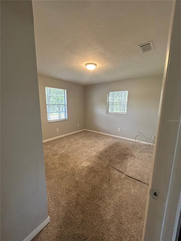 An empty bedroom with beige carpet, light gray walls, two windows, and a ceiling light — 2212 SE 36TH TERRACE UNIT A, GAINESVILLE, FL