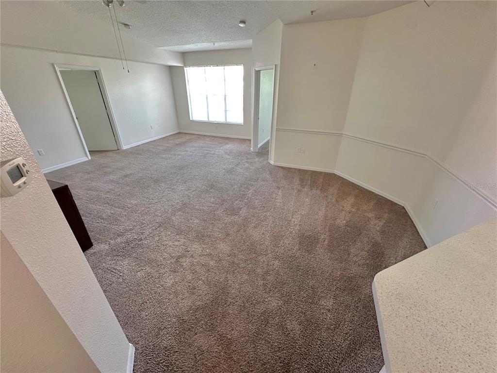 An empty room with beige carpet, white walls, a large window, and two doorways — 5554 METROWEST BOULEVARD UNIT 4-201, ORLANDO, FL