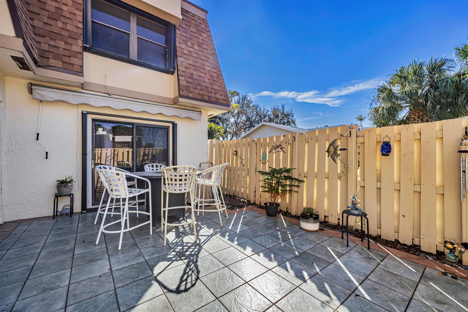 A tiled patio features a high-top table set and a wooden privacy fence outdoors — 825 NW 30th Avenue # A, Delray Beach FL 33445, DELRAY BEACH, FL