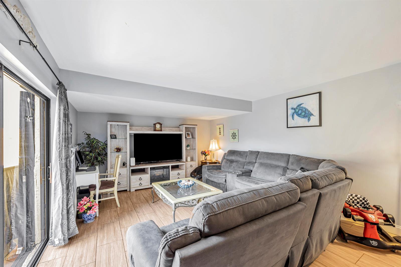 A living room features a grey sectional sofa, a television console, and tile flooring — 825 NW 30th Avenue # A, Delray Beach FL 33445, DELRAY BEACH, FL