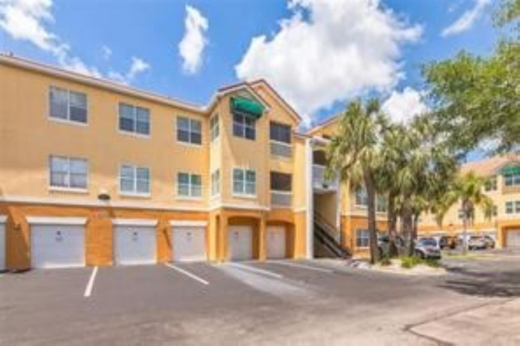A three-story apartment building with tan stucco walls and ground-level garage doors — 10764 70TH AVENUE UNIT 3305, SEMINOLE, FL