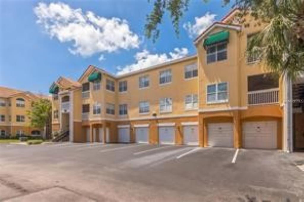 A multi-story apartment building with tan stucco walls and ground-level garages in a parking lot — 10764 70TH AVENUE UNIT 3305, SEMINOLE, FL
