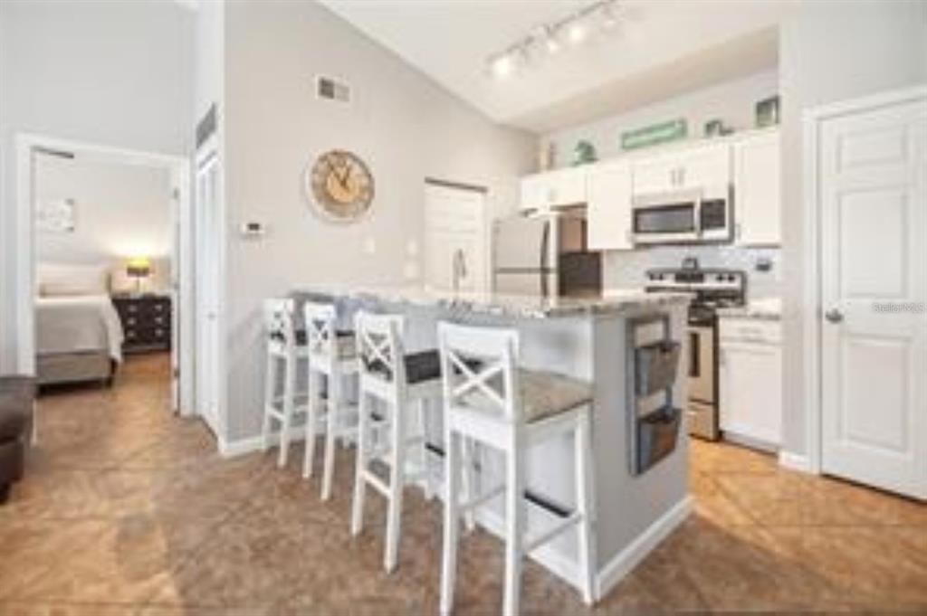 A kitchen with white cabinets, a granite-topped island, and four white bar stools — 10764 70TH AVENUE UNIT 3305, SEMINOLE, FL