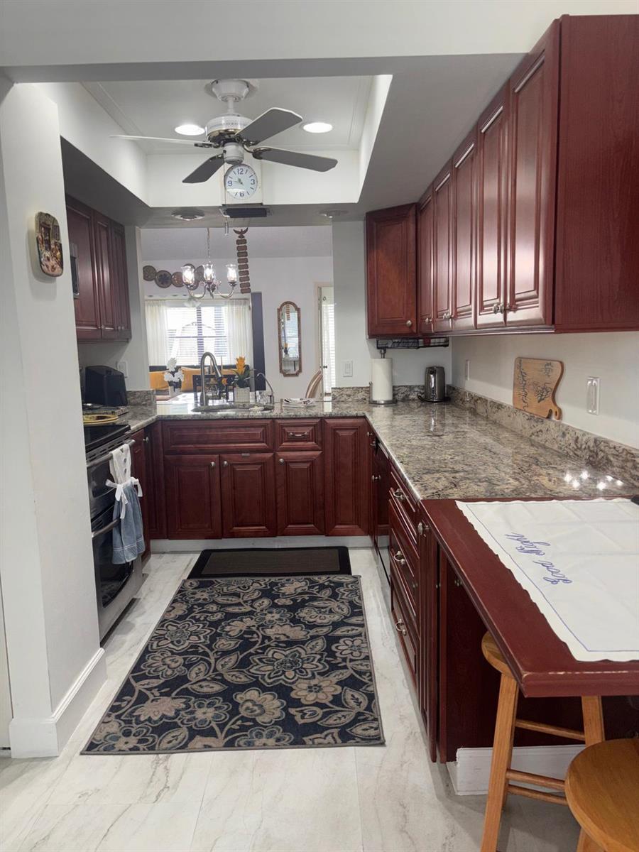A galley kitchen features dark wood cabinets, granite countertops, and a patterned area rug — 6285 Tall Cypress Circle, FL 33463, FL