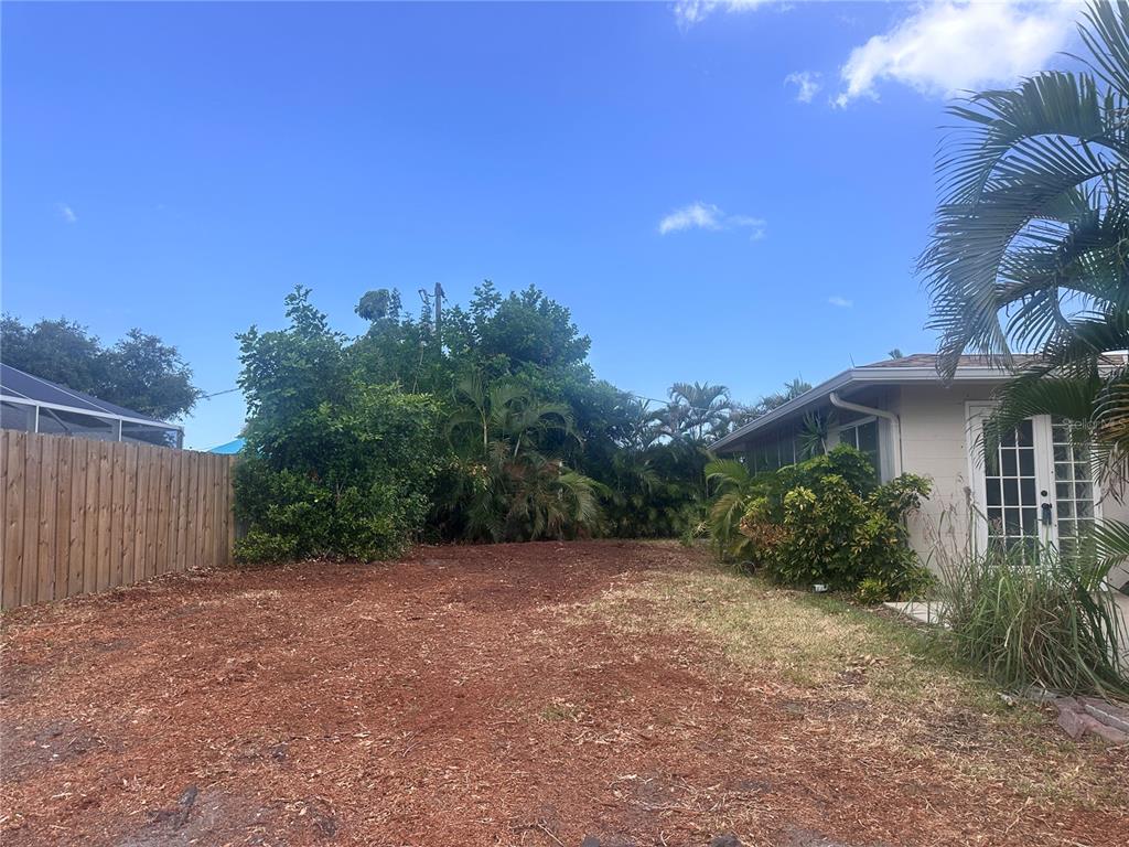 A backyard area features a wood fence, mulch ground cover, and a house with glass doors — 448 REDWOOD ROAD, VENICE, FL