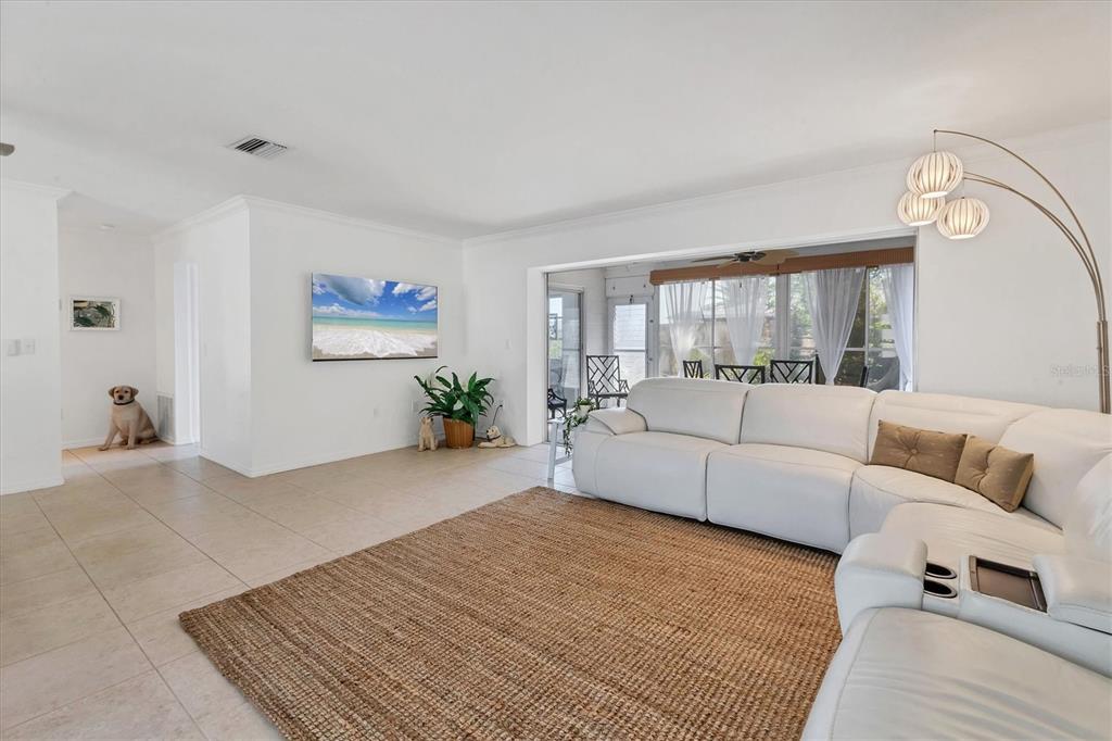 A bright living room features white walls, tile flooring, a large sectional sofa, and a rug — 448 REDWOOD ROAD, VENICE, FL