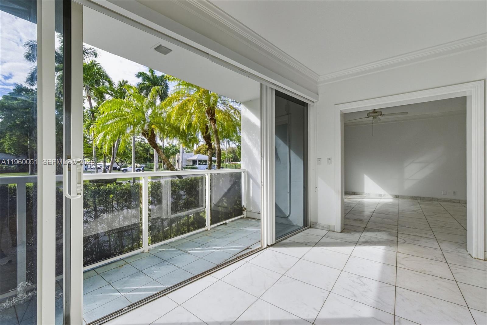 A balcony with a glass railing overlooks palm trees, adjacent to an indoor tiled room — 1 Harbour Way # 108, Bal Harbour FL 33154, BAL HARBOUR, FL