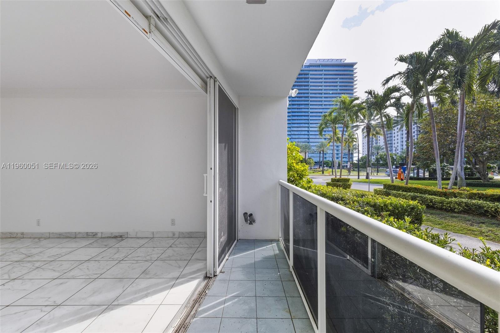 A balcony with white tile floors, a glass railing, and a view of palm trees — 1 Harbour Way # 108, Bal Harbour FL 33154, BAL HARBOUR, FL