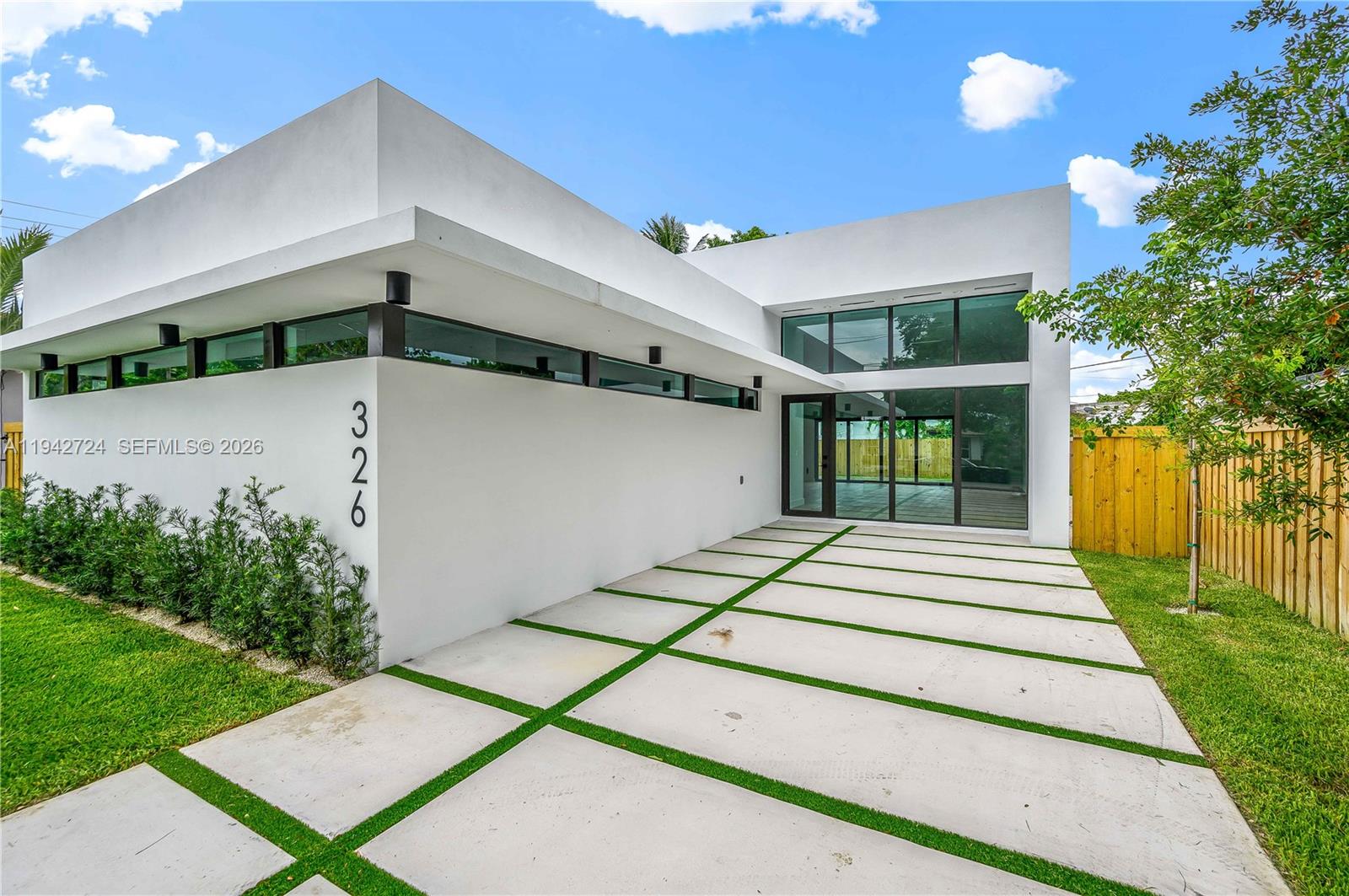 A modern white house exterior features a concrete driveway with grass strips and large windows — 326 NW 40th St, Miami FL 33127, MIAMI, FL