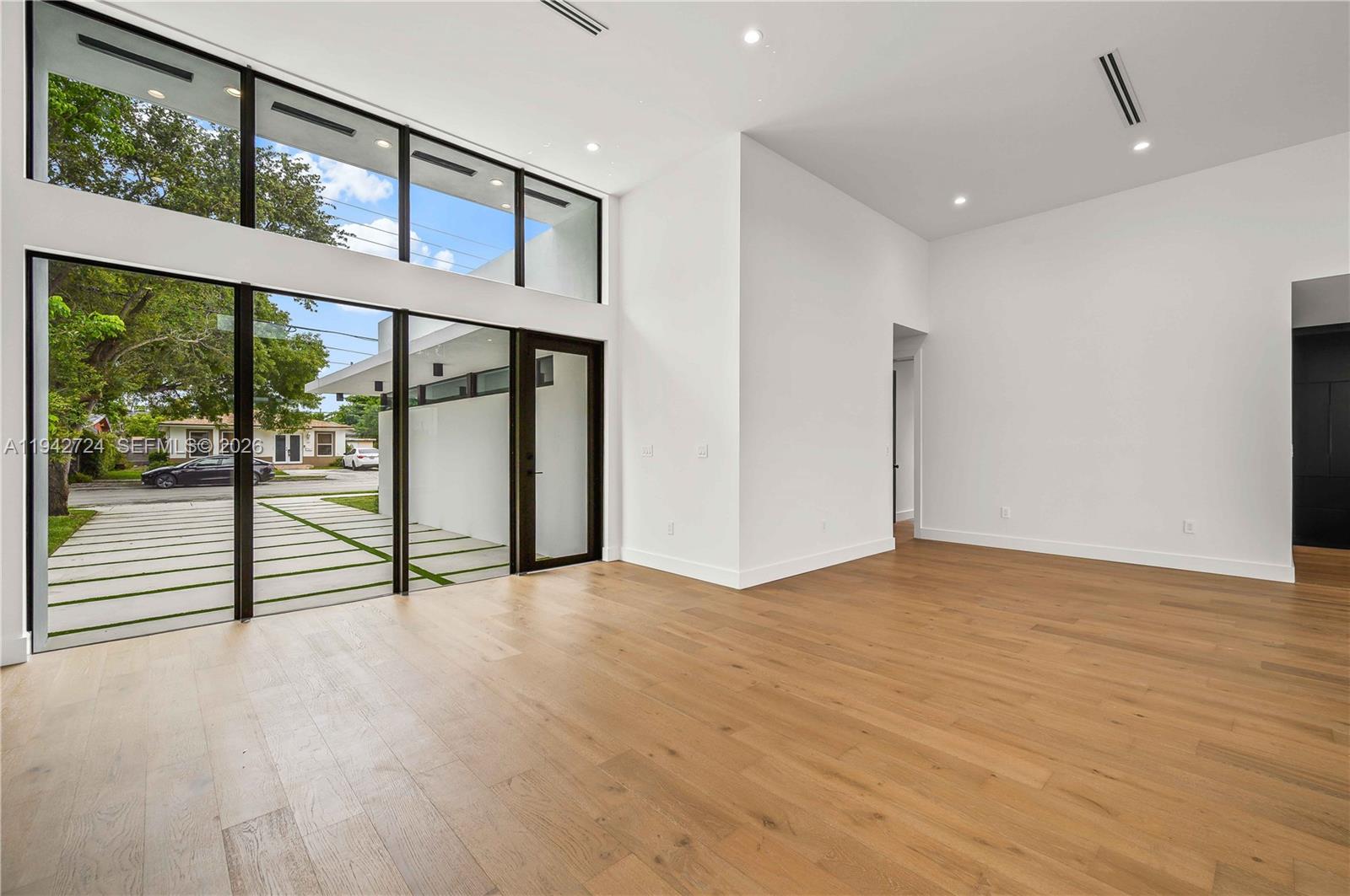 A bright, minimalist living room features floor-to-ceiling windows, light wood flooring, and white walls — 326 NW 40th St, Miami FL 33127, MIAMI, FL