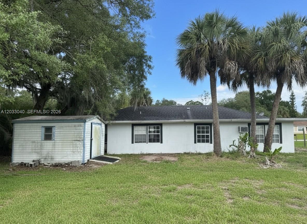 A white single-story house with a shed and palm trees in the backyard — 4029 E Sunflower Cir, La Belle FL 33935, LA BELLE, FL