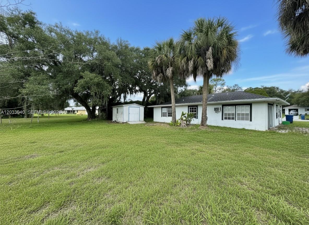 A white single-story house with a small shed and palm trees in a grassy yard — 4029 E Sunflower Cir, La Belle FL 33935, LA BELLE, FL