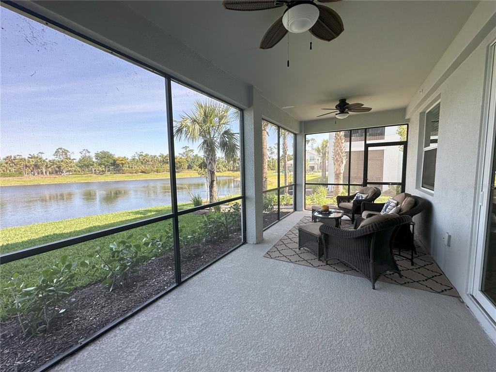 A screened-in patio features wicker furniture, a ceiling fan, and a view of a lake — 14649 SYCAMORE COURT UNIT 2912, PUNTA GORDA, FL