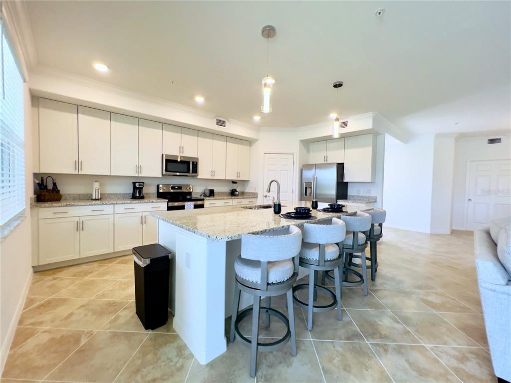 A kitchen features white cabinetry, granite countertops, a central island with bar stools, and tile flooring — 14649 SYCAMORE COURT UNIT 2912, PUNTA GORDA, FL