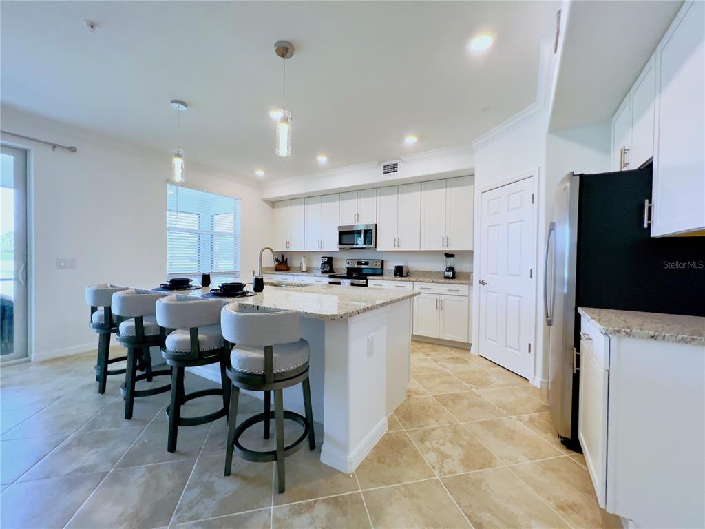 A kitchen features white cabinets, granite countertops, a central island with bar stools, and tile flooring — 14649 SYCAMORE COURT UNIT 2912, PUNTA GORDA, FL