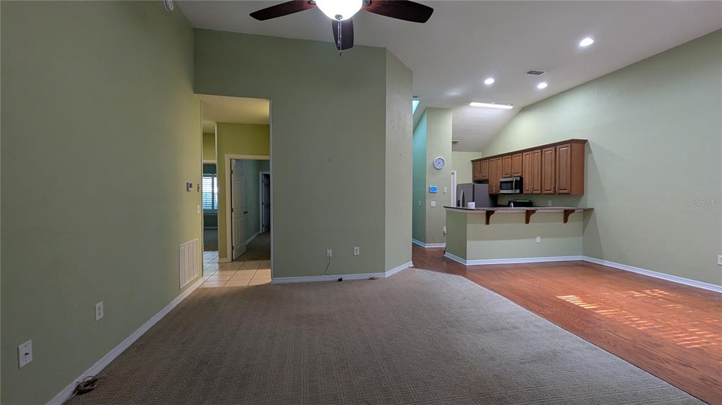 A living room with carpeted floors transitions into a kitchen with wood cabinets and laminate flooring — 13200 W NEWBERRY ROAD UNIT Z144, NEWBERRY, FL